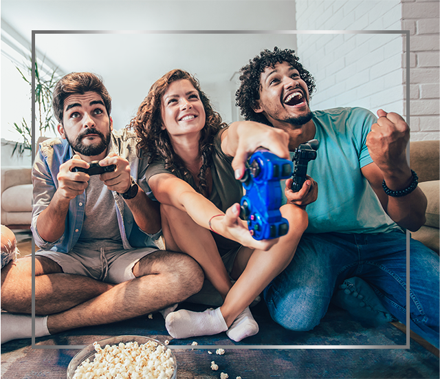 Skupina mladých, usmívajících se lidí sedí na podlaze a hraje videohry, jsou šťastní po léčbě plísňové infekce kůže přípravkem Canesten krém